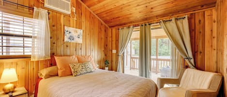 A wooden cabin bedroom with a bed, a chair, a window with curtains, and a wall-mounted heater.