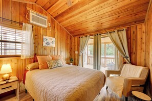 Une chambre dans une cabane en bois, avec un lit, une chaise, une fenêtre avec des rideaux et un radiateur fixé au mur.