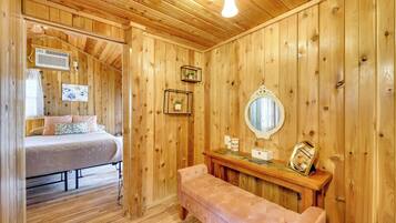 A wooden room with a bed, a bench, a mirror, and a wall-mounted shelf.