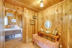 Ein Zimmer mit Holzboden, einem Bett, einer Bank, einem Spiegel und einem an der Wand befestigten Regal.
