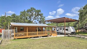 A wooden cabin with a porch and a covered area, adjacent to a Jayco RV.