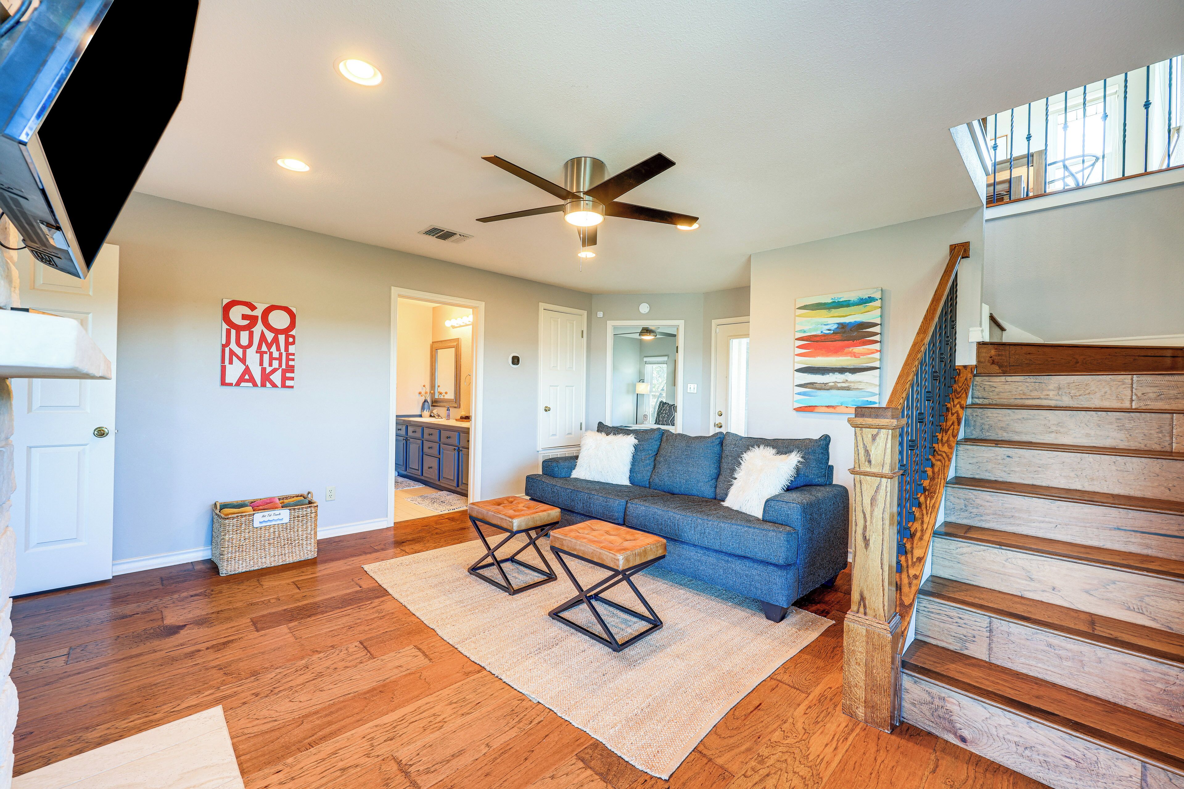 A spacious living room with hardwood floors, a blue sofa, a wooden staircase, and a ceiling fan.