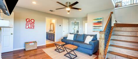 A spacious living room with hardwood floors, a blue sofa, a wooden staircase, and a ceiling fan.
