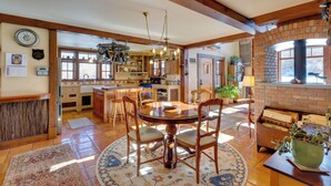 A spacious kitchen with wooden beams, a dining area with a round table, and a brick fireplace. - Solar-powered Home w/ Mtn Views 33 Mi to Telluride (Placerville)