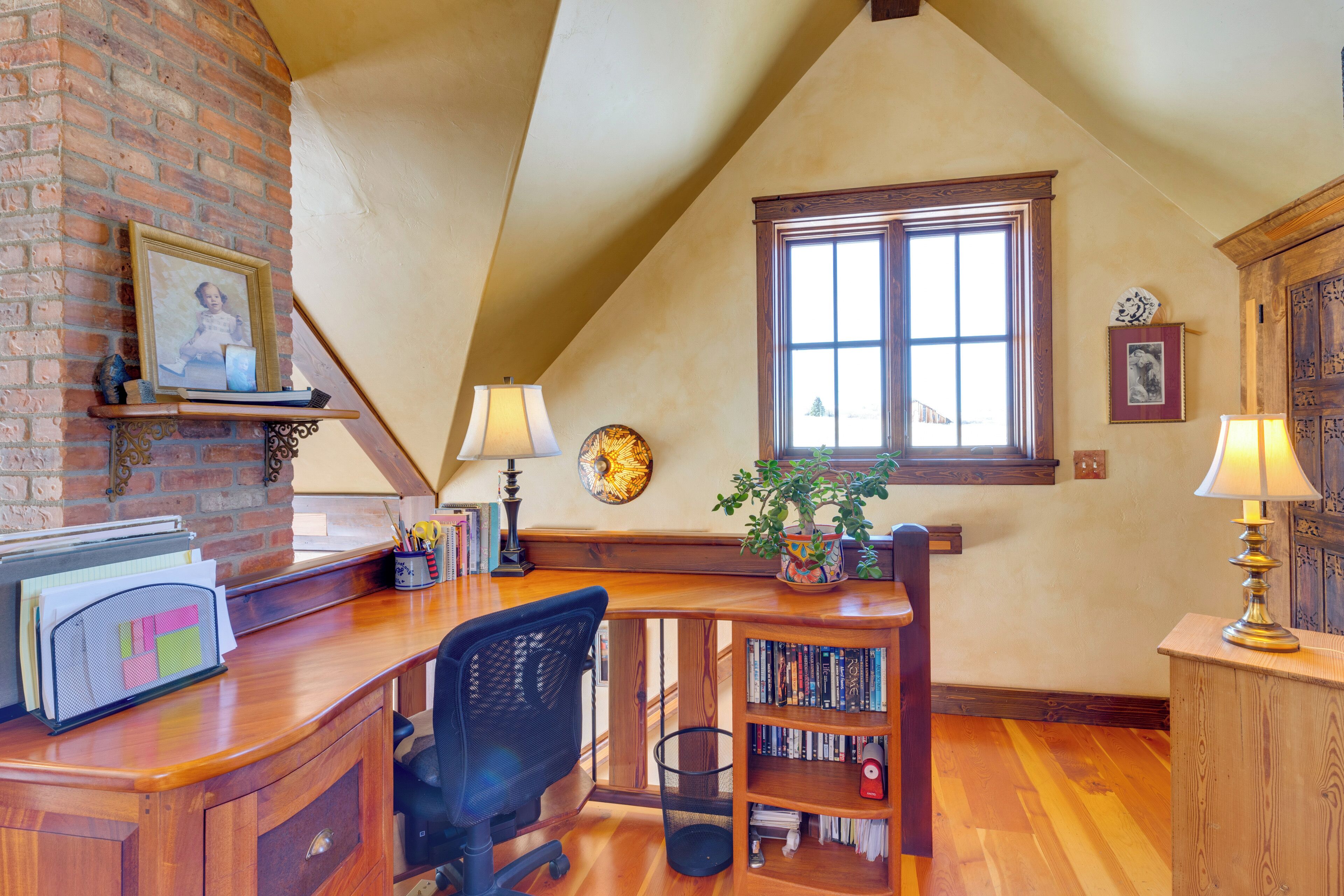 A home office with a desk, chair, bookshelf, and a large window.