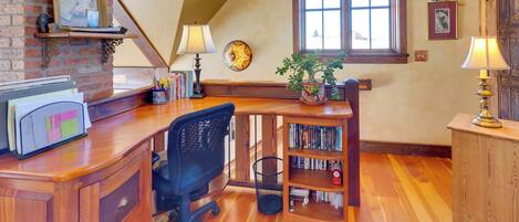A home office with a desk, chair, bookshelf, and a large window.