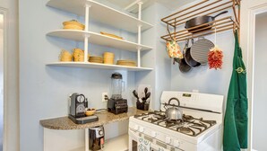 Una cocina con alacenas blancas, estufa a gas, cafetera y un colgador para ollas.