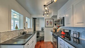 A modern kitchen with white cabinets, a black countertop, a stainless steel sink, a stove, and a microwave. - Chic Downtown Home w/ Grill, Steps to Main Street! (Buena Vista)