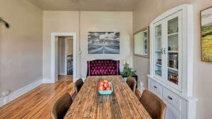 A dining room with a wooden table, a fruit bowl, and a velvet-upholstered headboard. - Chic Downtown Home w/ Grill, Steps to Main Street! (Buena Vista)