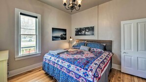 A bedroom with a large bed, a chandelier, a window, and two framed pictures on the wall. - Chic Downtown Home w/ Grill, Steps to Main Street! (Buena Vista)