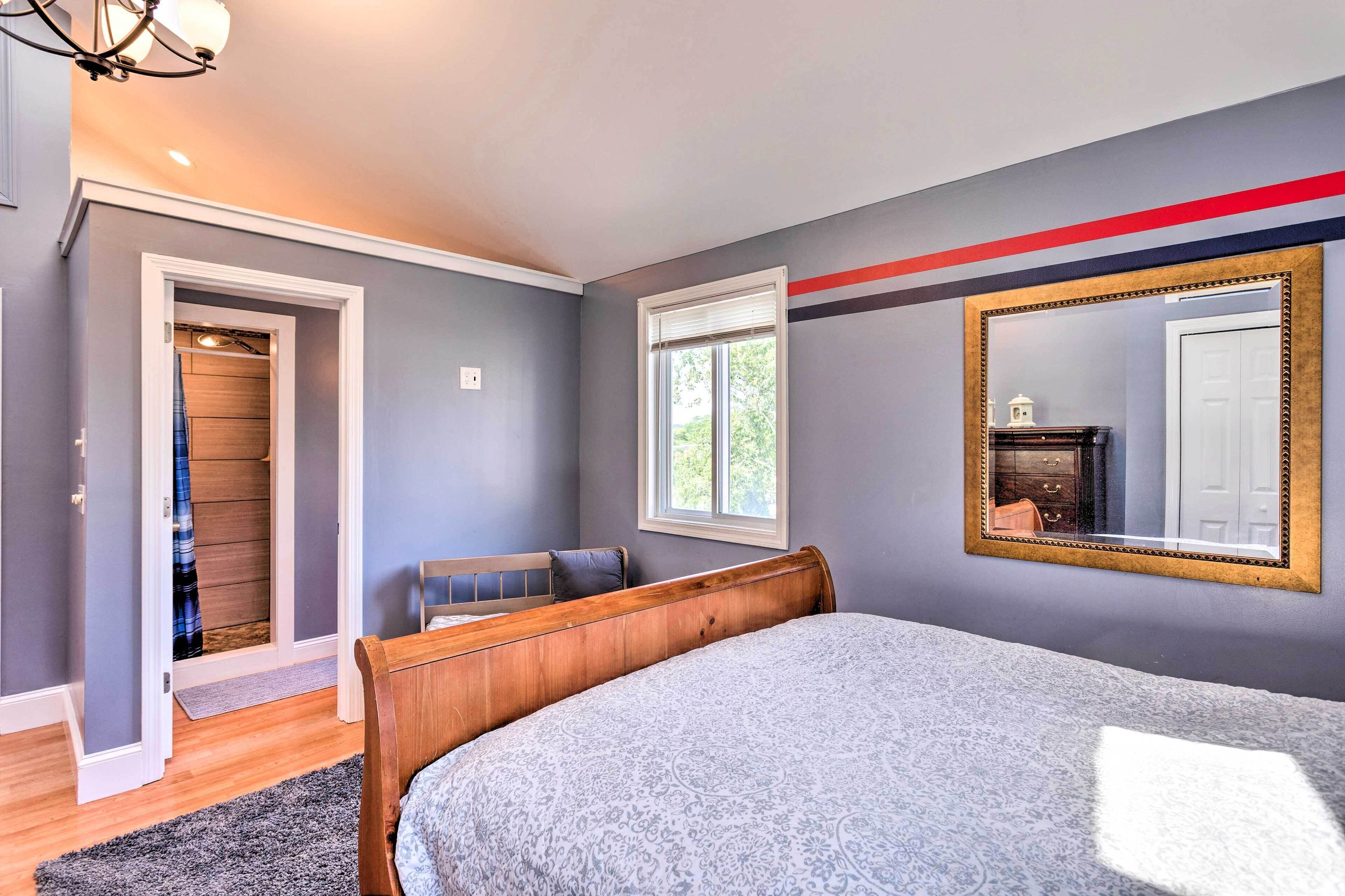 A bedroom with a bed, a window, a mirror, and a door leading to a hallway.