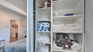 Un placard bien rangé, avec des étagères où sont pliés des vêtements, une valise et une boîte étiquetée « Chicco pour enfants ».