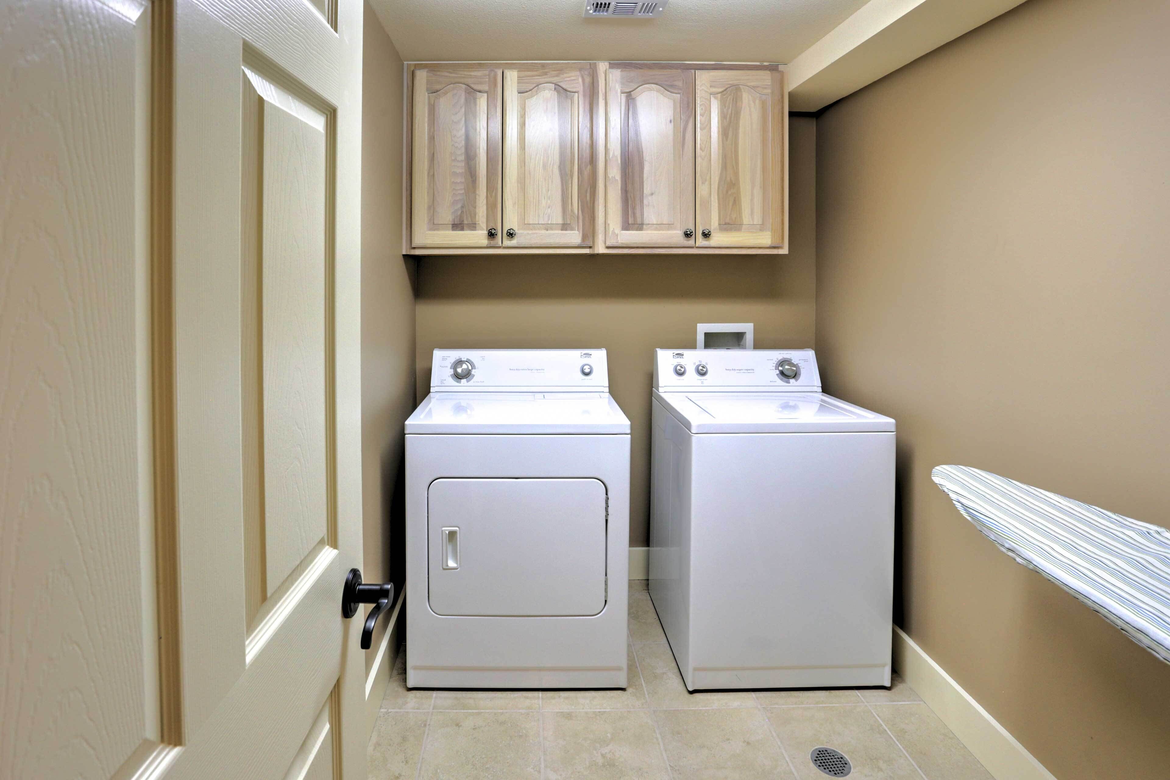 A laundry room with two white front-loading washers and dryers, wooden cabinets above, and beige walls.