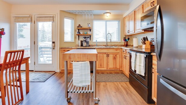 Una cocina moderna con armarios de madera, un refrigerador de acero inoxidable, horno empotrado y una pequeña isla con una toalla.