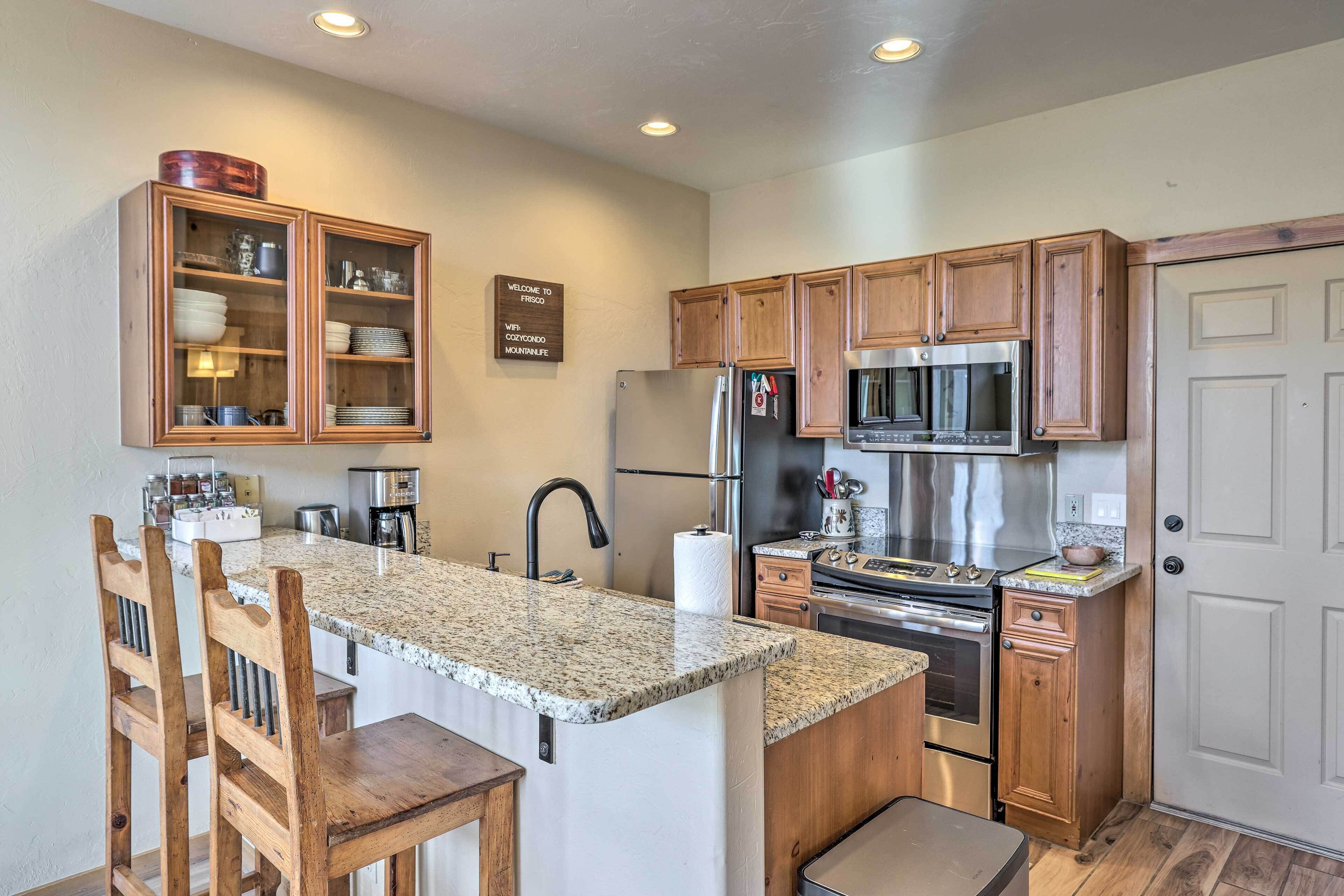 A kitchen with wooden cabinets, a granite countertop, a stainless steel refrigerator, a microwave, and a coffee machine.