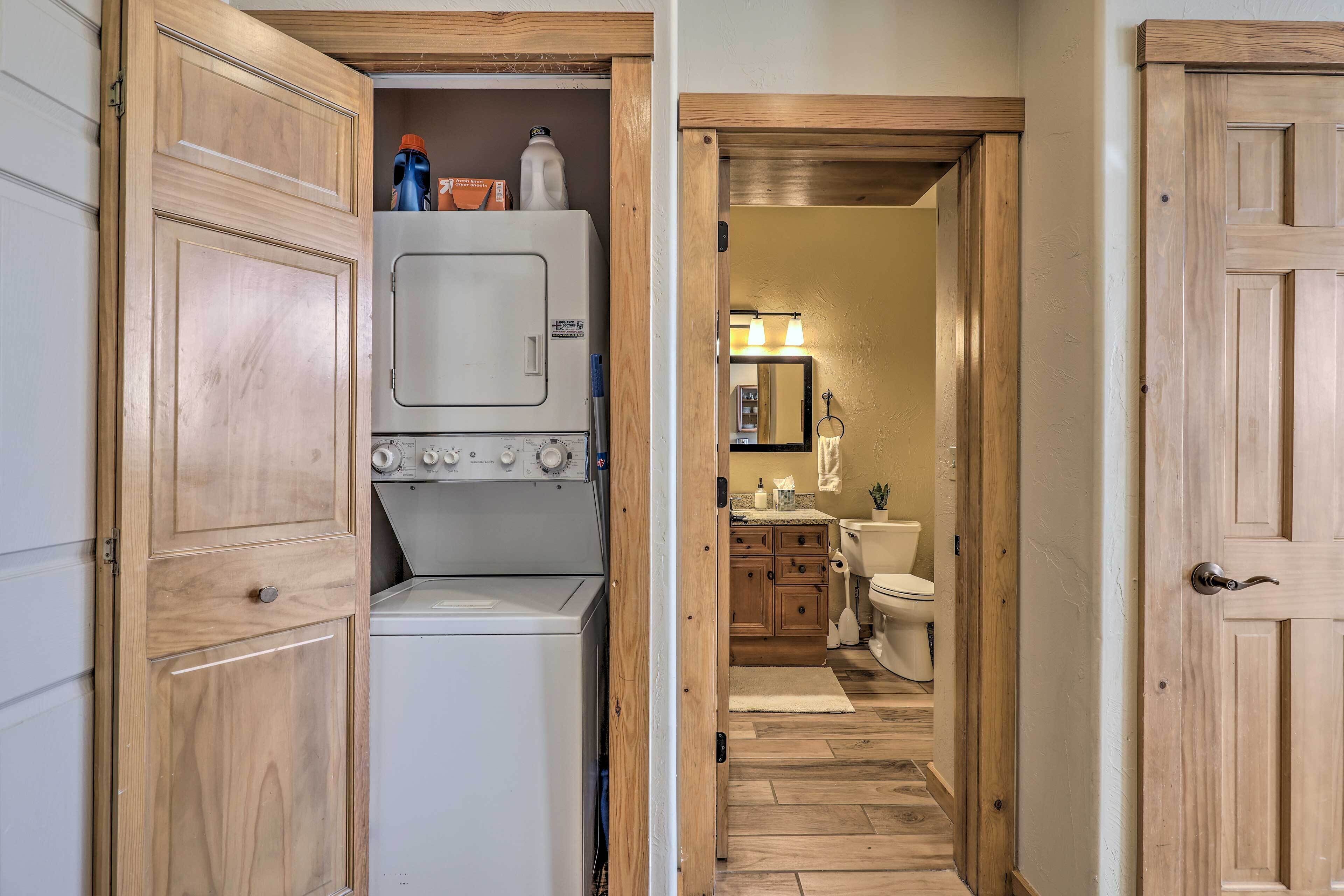 A laundry room with stacked washer and dryer, wooden cabinets, and a hallway leading to a bathroom with a toilet and sink.