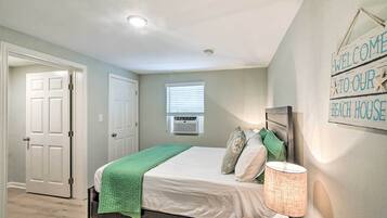 A bedroom with a bed, a green throw blanket, a lamp, and a 'Welcome to our Beach House' sign.