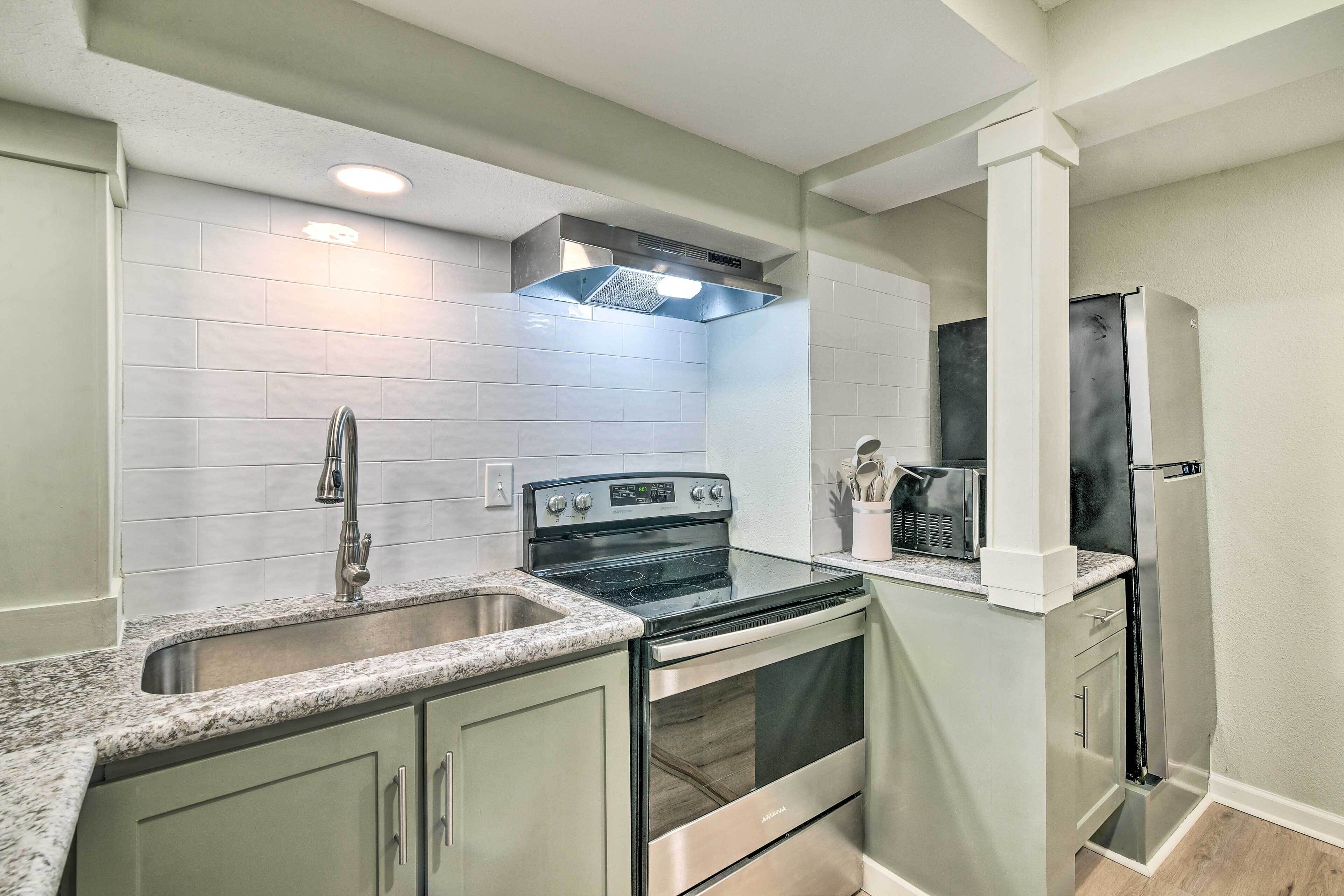 A compact kitchen with a stainless steel stove, oven, and refrigerator, a granite countertop, and white subway tiles.