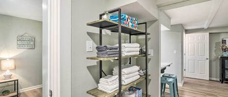 A laundry room with a metal shelving unit holding folded towels and a basket of laundry supplies.