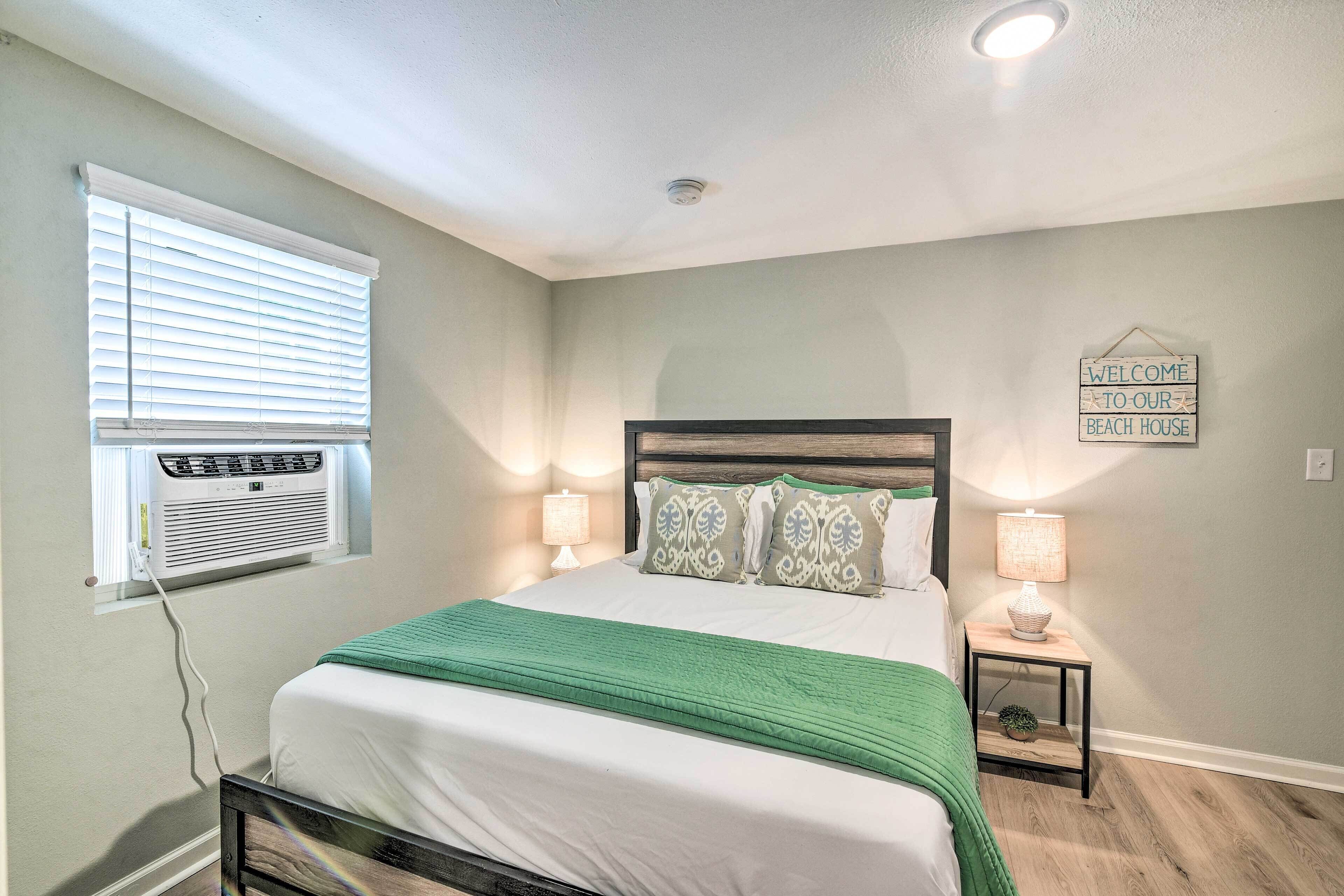 A bedroom with a bed, bedside lamps, a wall-mounted air conditioner, and a welcome sign.