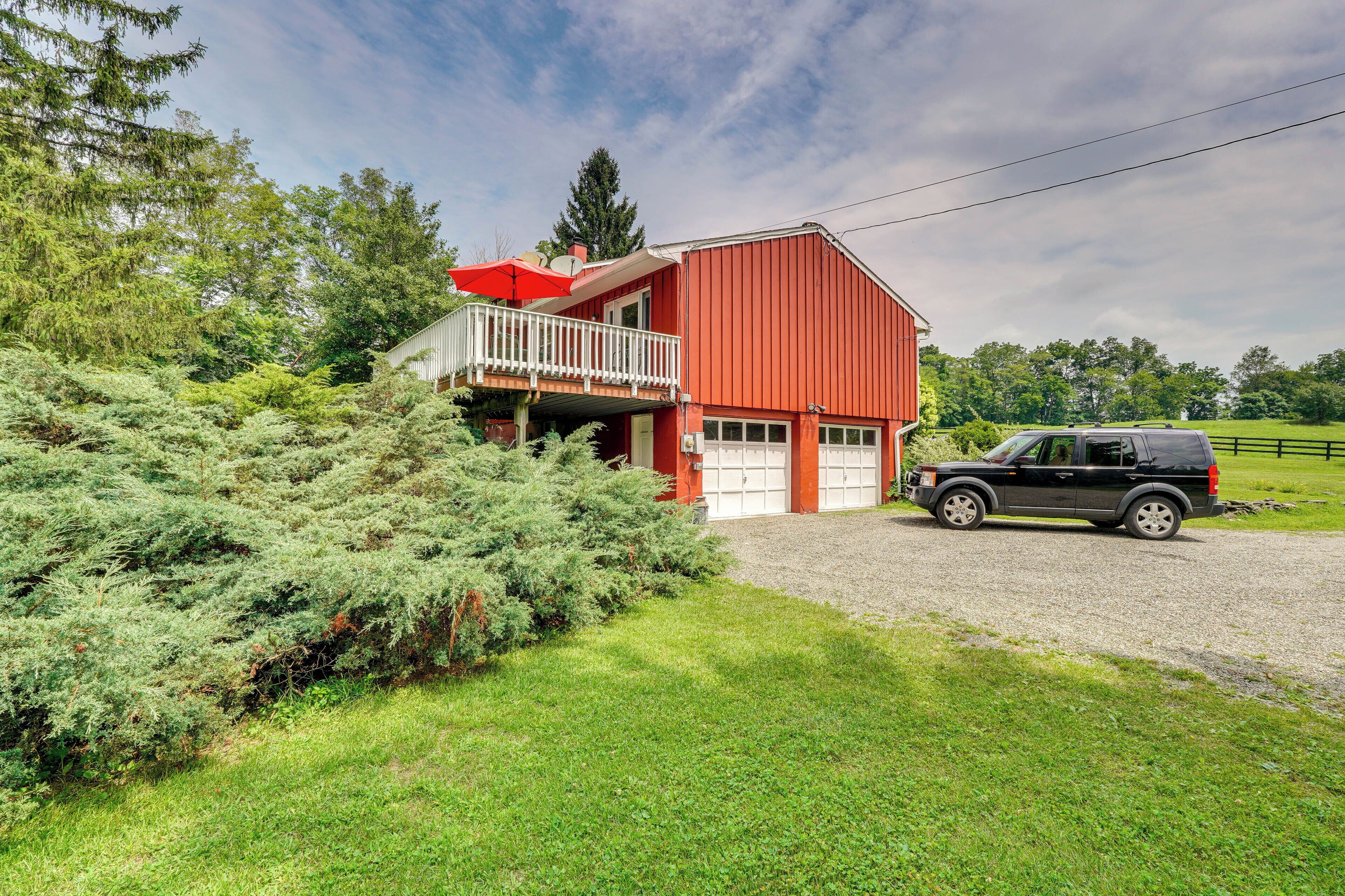 A red barn with a white balcony, a gravel driveway, and a parked SUV.