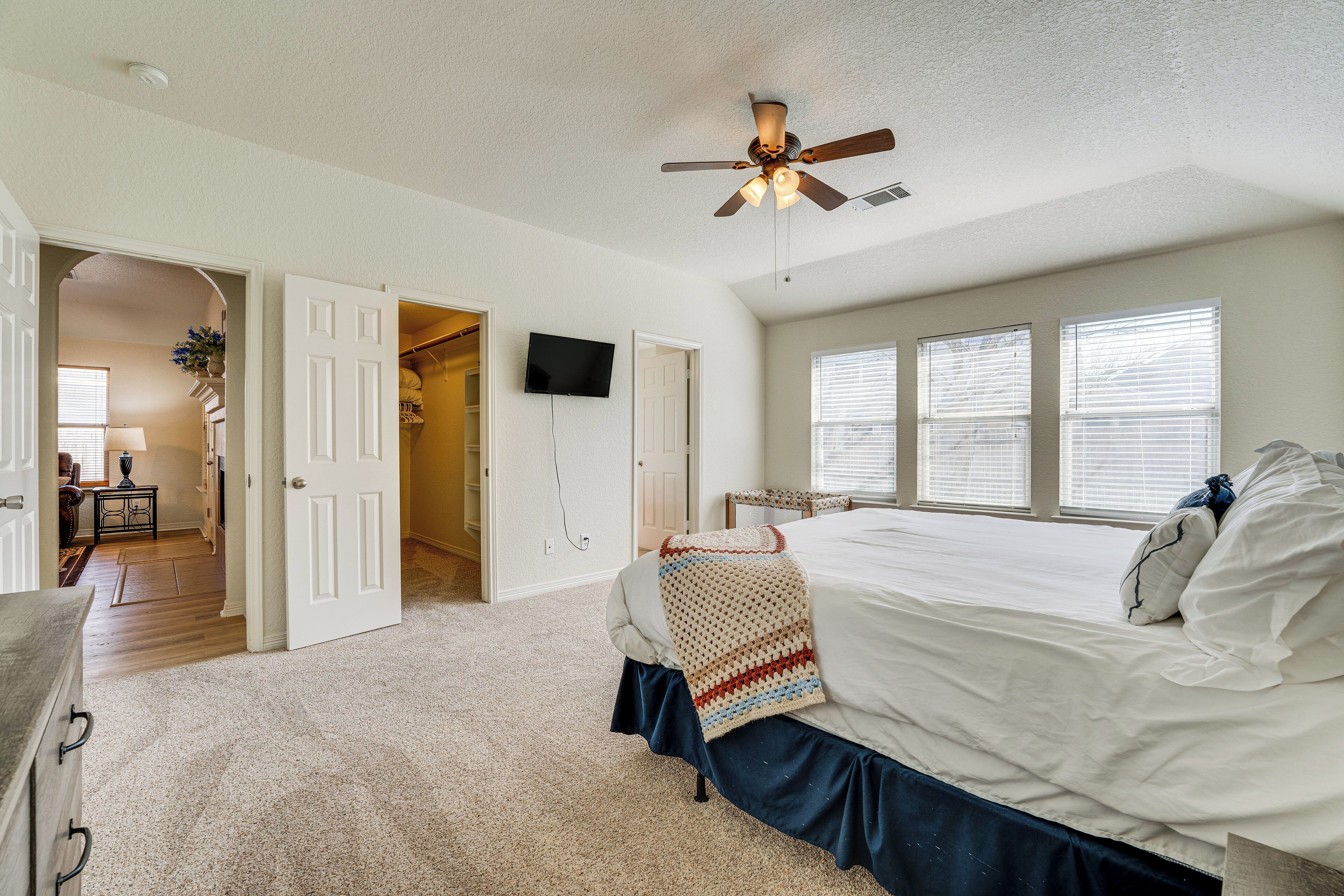 A bedroom with a large bed, a ceiling fan, and a TV on the wall.