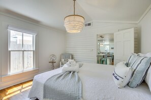 Une chambre avec un grand lit, un lustre, une fenêtre avec des stores et un ventilateur.