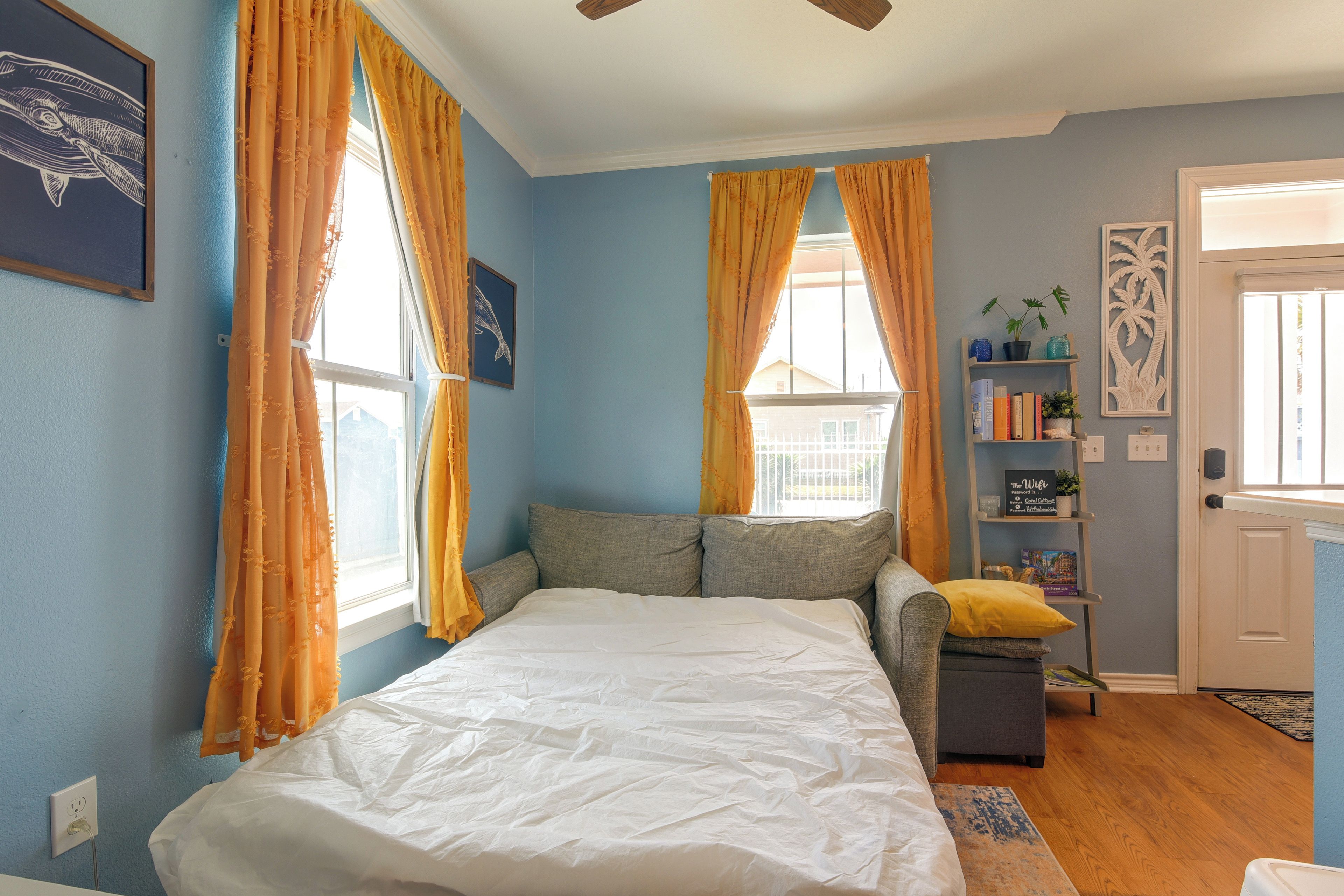 A bedroom with a bed, two windows with curtains, a bookshelf, and a door.