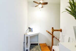 Una habitación con ventilador de techo, escritorio con lámpara, una planta y una escalera.