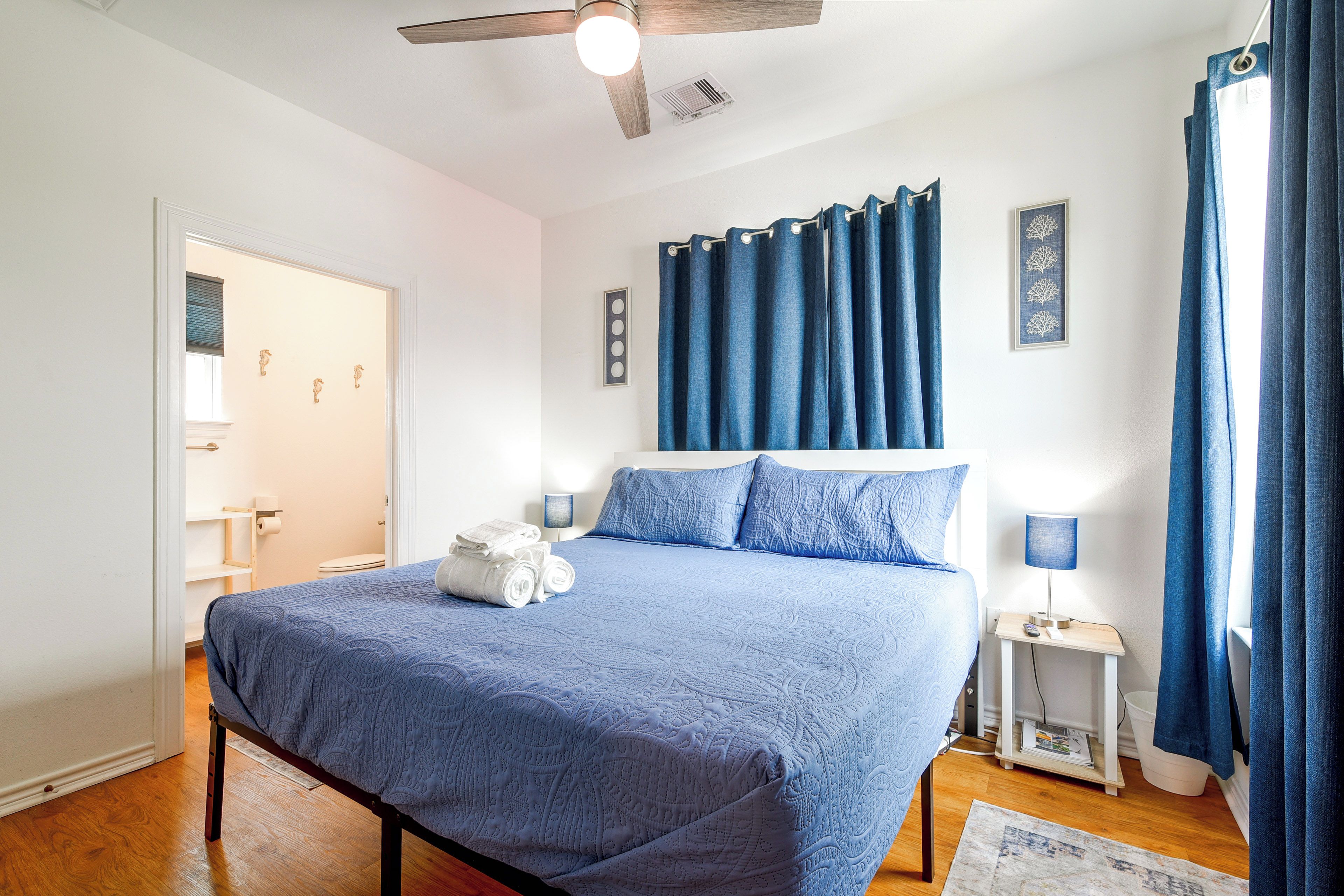 A bedroom with a bed, a nightstand, a lamp, a ceiling fan, and a bathroom door.