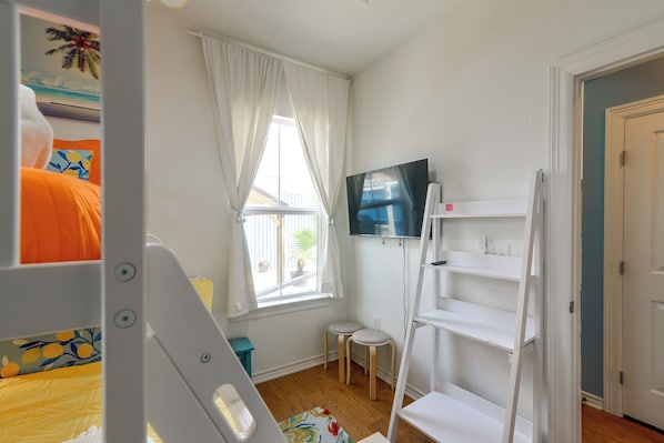 A child's room with a bunk bed, a small stool, a TV on a stand, and a window with curtains.