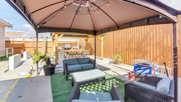 Ein überdachter Patio-Bereich mit Gartenmöbeln, einem Esstisch und einem großen Sonnenschirm, der Schatten spendet.