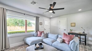 A modern living room with a sectional sofa, a ceiling fan, and a dining area with a table and chairs.