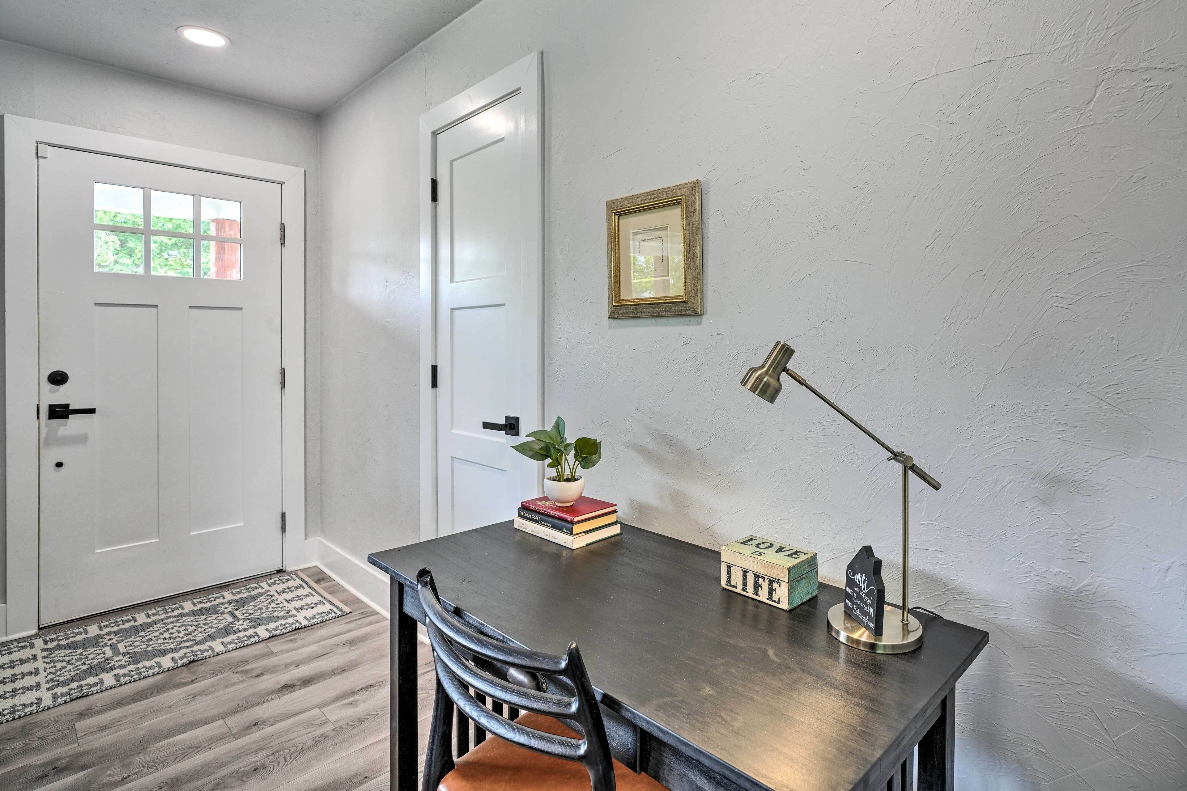 A dining area with a table, chairs, a plant, a framed picture, and a desk lamp.