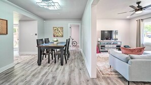 A modern living room with a sofa, a dining area with a table and chairs, a ceiling fan, and a TV.