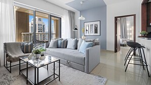A modern living room with a grey sofa, a glass coffee table, and a view of a cityscape through large windows. - Silkhaus 29 Boulevard, Downtown Dubai (Dubai)