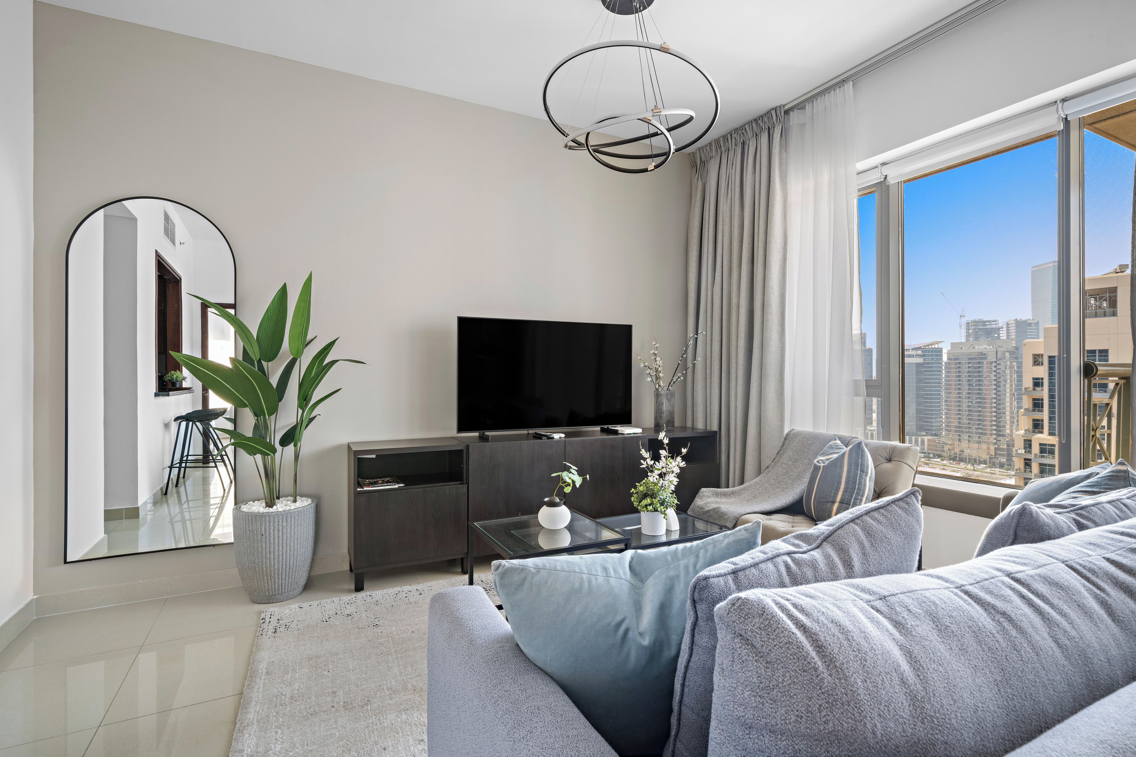 A modern living room with a large flat-screen TV, grey sofas, a coffee table, and a potted plant.