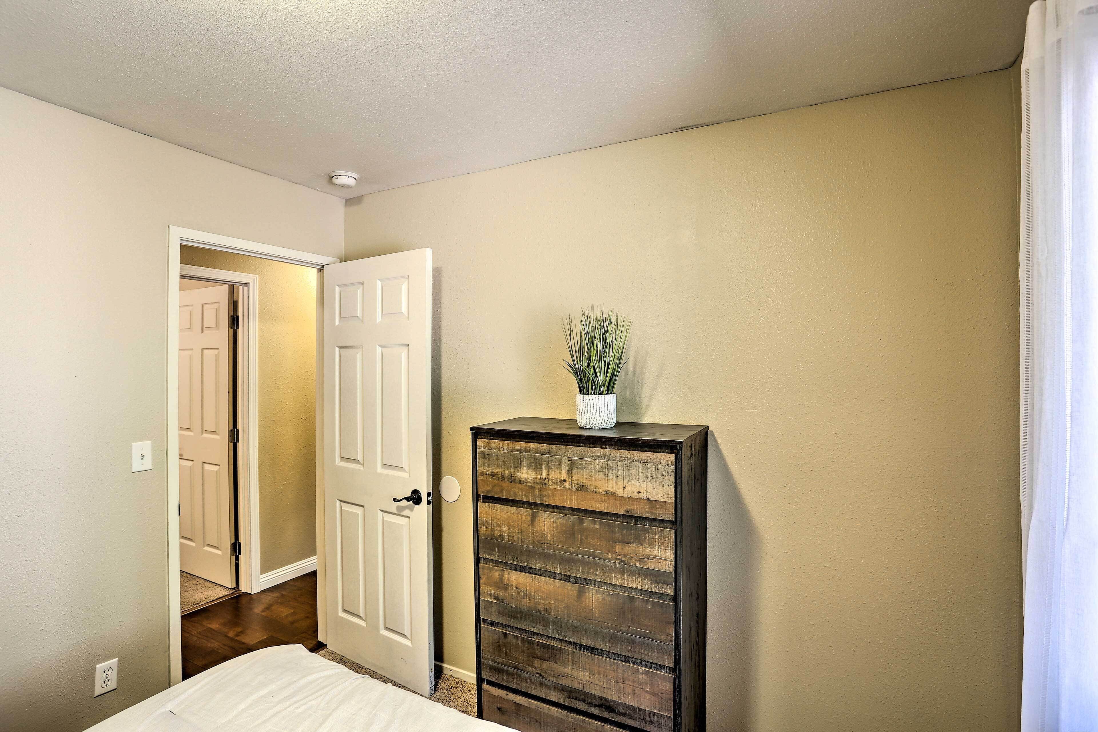 A bedroom with a bed, a dresser, and a door leading to another room.