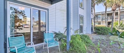 A building with a covered patio area featuring two blue chairs and a glass door entrance.