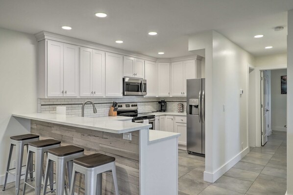 A modern kitchen with white cabinets, a central island with stools, stainless steel appliances, and recessed ceiling lights.