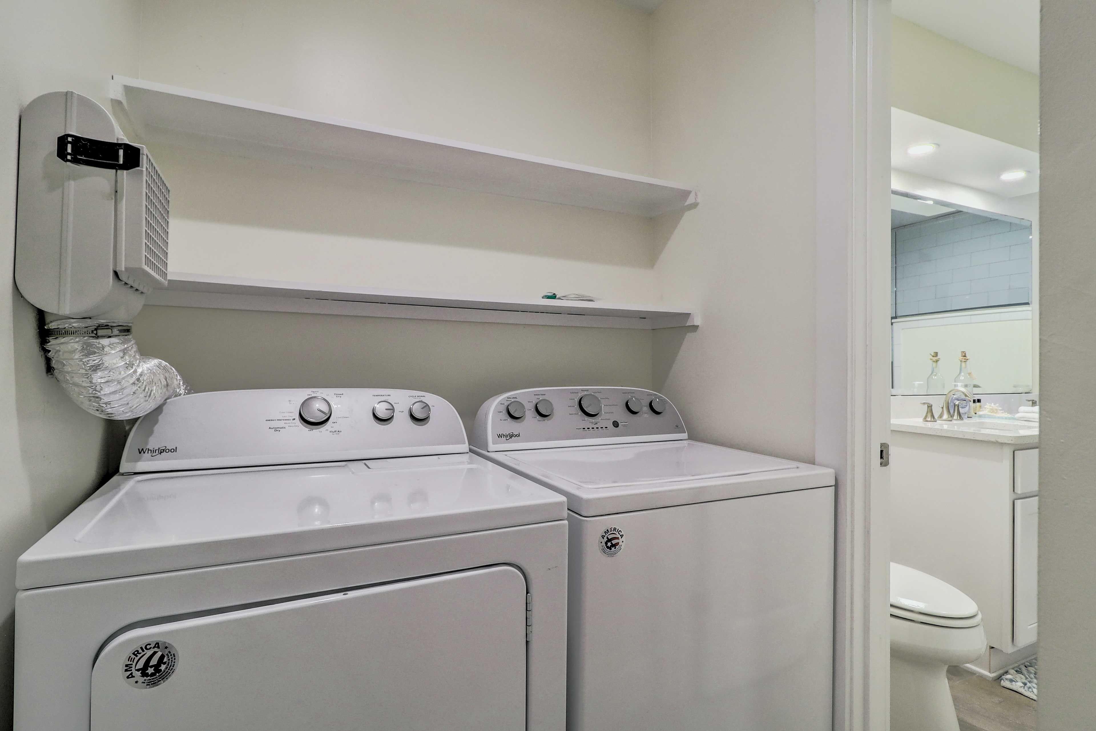 A laundry room with two Whirlpool washers and a dryer, a white ceiling, and a visible bathroom with a toilet and sink.