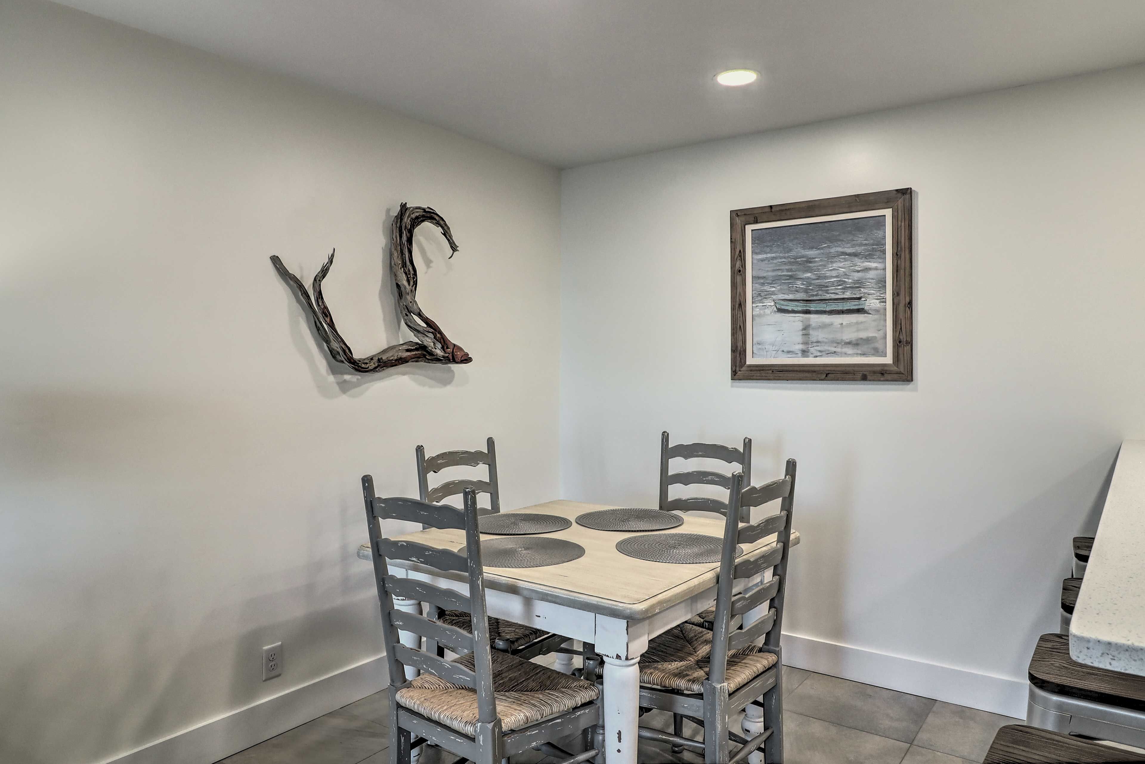 Un coin repas avec une table blanche et quatre chaises, un tableau encadré au mur et un élément de décoration murale original.