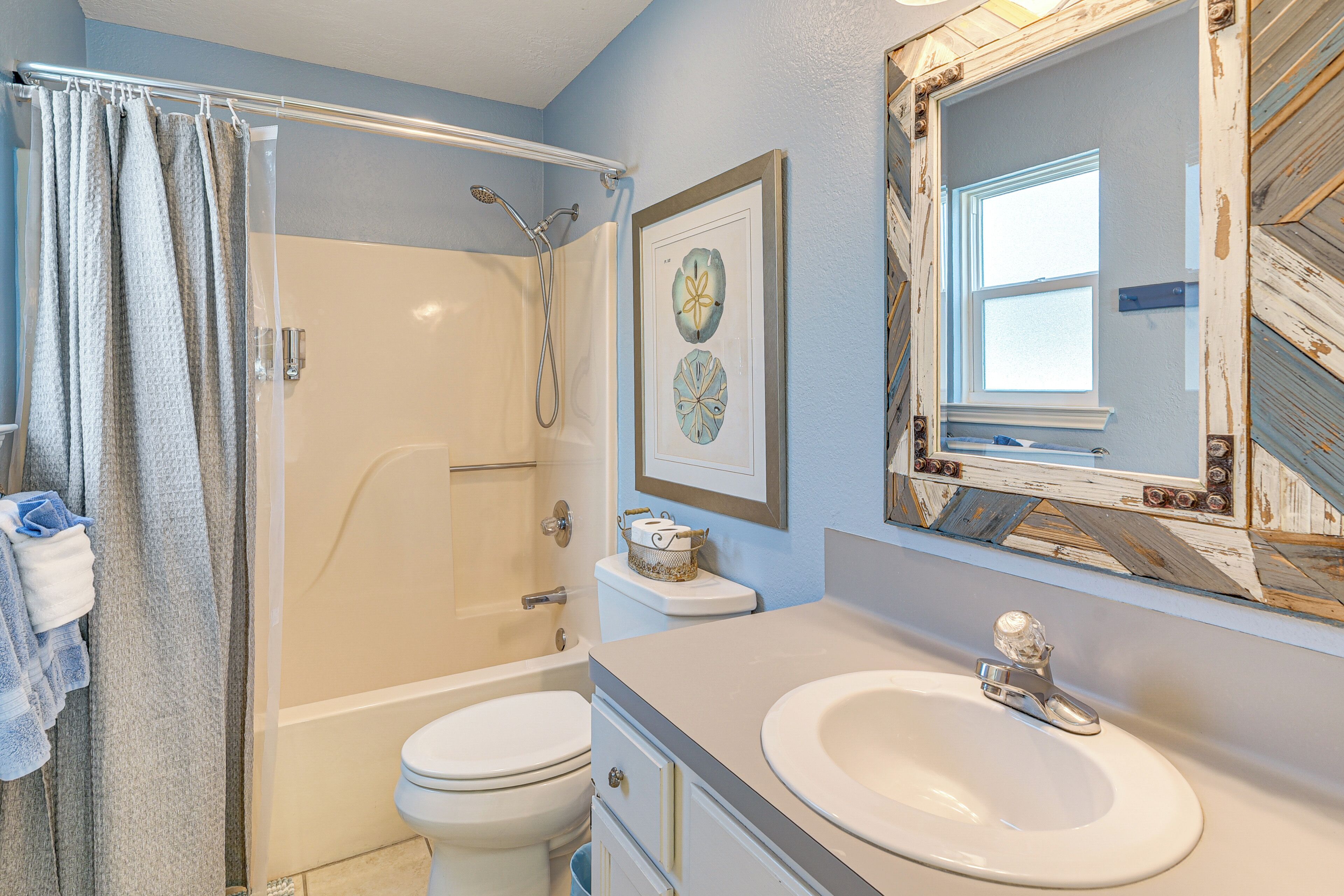 A bathroom with a shower, toilet, sink, and a framed picture on the wall.