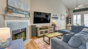 A living room with a fireplace, a large flat-screen TV, a sofa, and a ceiling fan. - Ocean-view Beach House in Galveston, Dogs Welcome! (Galveston)