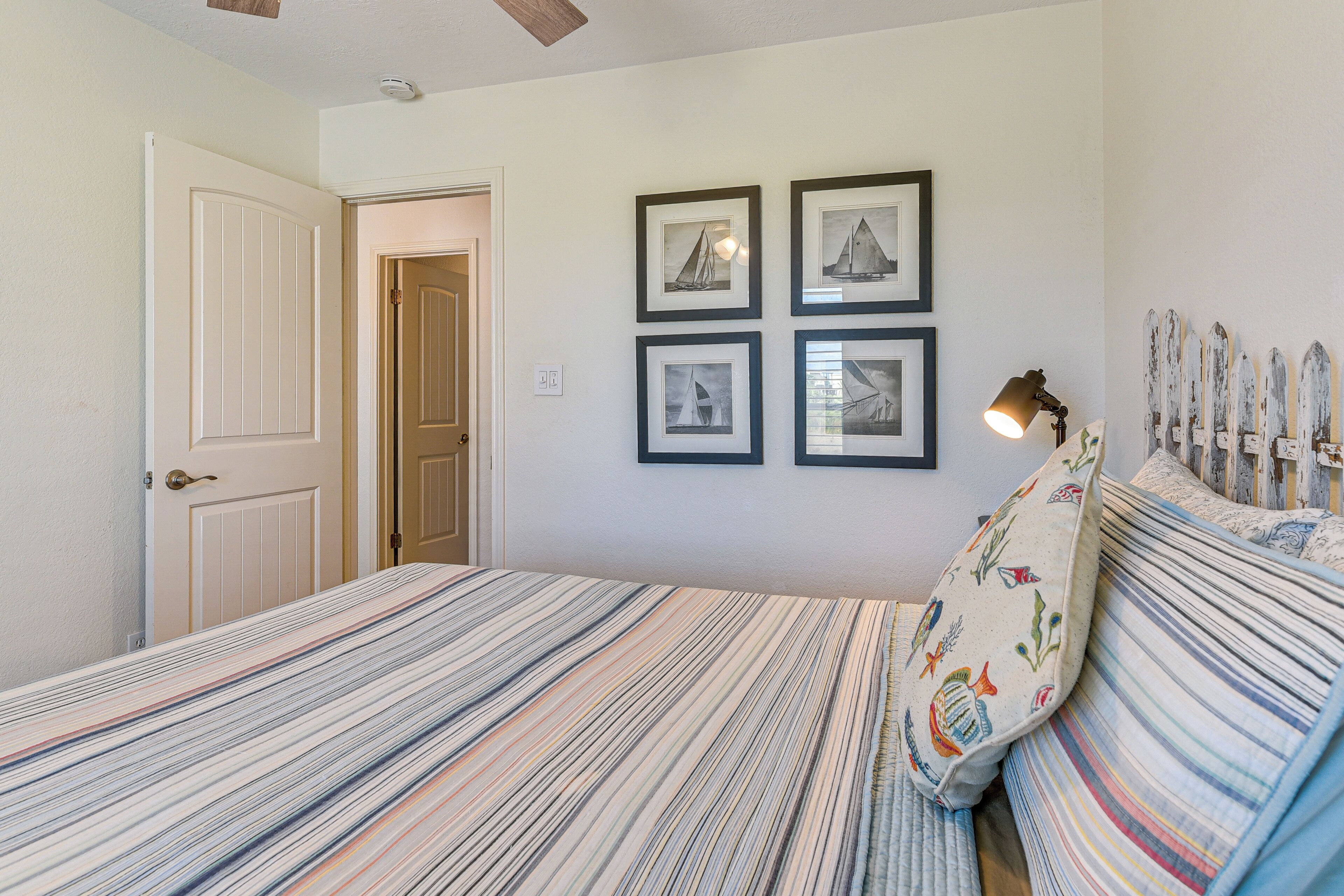 A bedroom with a striped bedspread, a door, and four framed pictures on the wall.