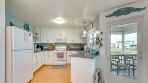 A kitchen with white cabinets, a microwave, and a stove. There is a wooden floor and a view of the outside through a glass door. - Pet-friendly Condo w/ Seasonal Pool in Galveston! (Galveston)