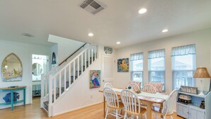 A dining area with a wooden table and white chairs, a staircase with white railings, and a sign indicating 'BEACH'. - Pet-friendly Condo w/ Seasonal Pool in Galveston! (Galveston)