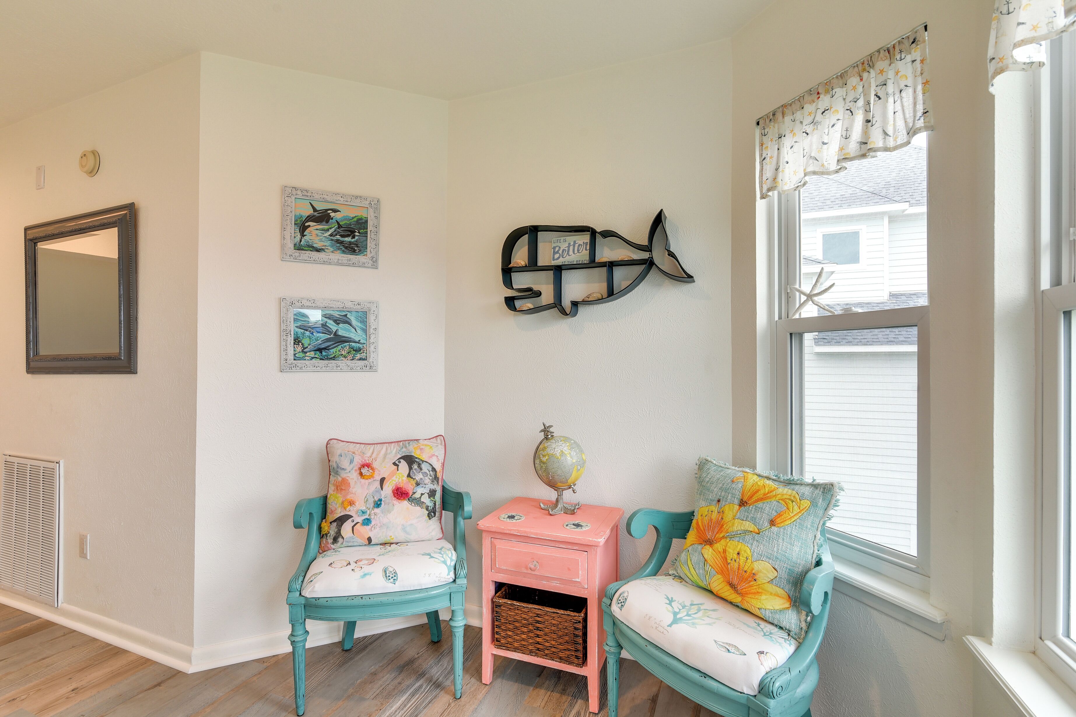 A room with two teal chairs, a pink side table with a globe, and wall art including a fish and marine-themed pictures.