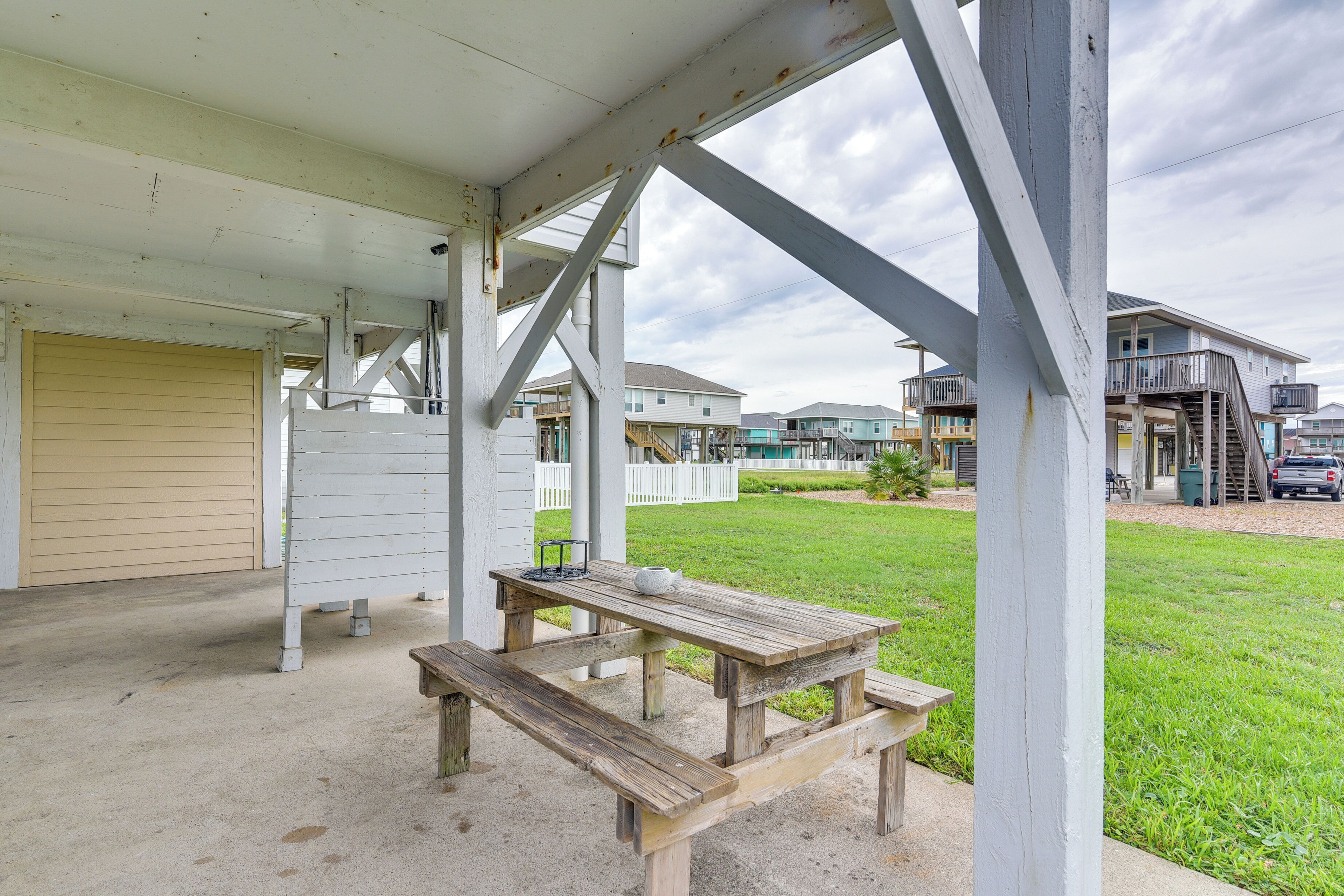 A covered outdoor area with a picnic table and benches, a garage door, and houses in the background.