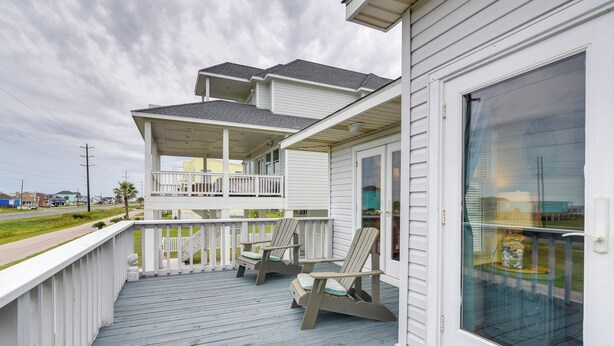 A covered deck with Adirondack chairs and a glass door. - Pet-friendly Condo w/ Seasonal Pool in Galveston! (Galveston)